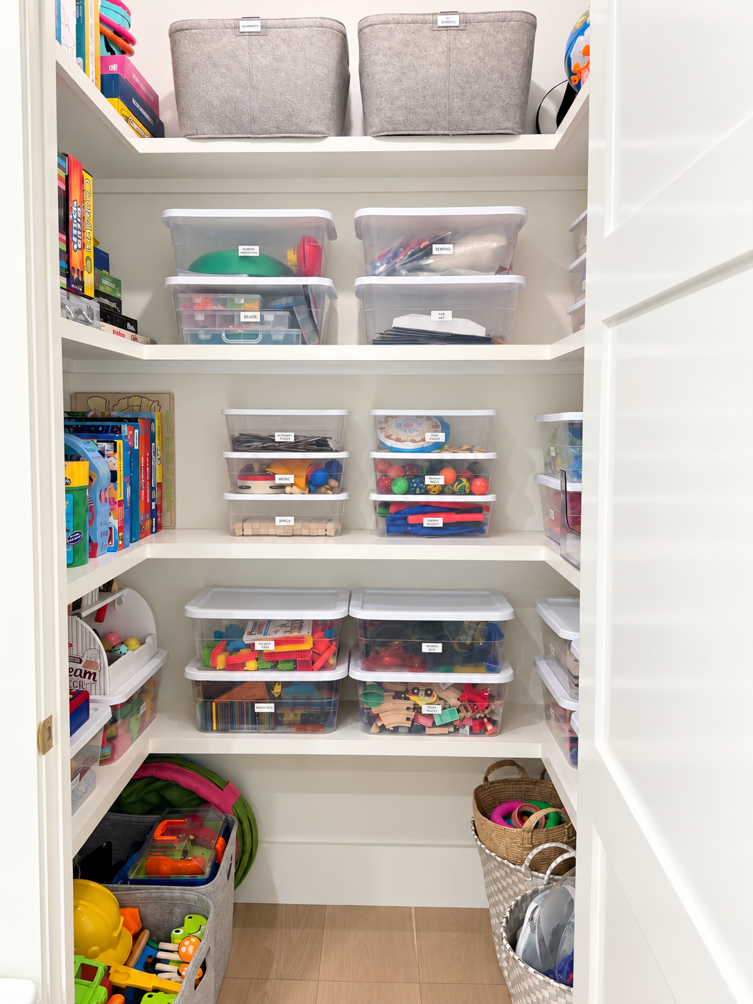 Organized playroom closet with labeled bins of toys and games sorted by activity on white shelves