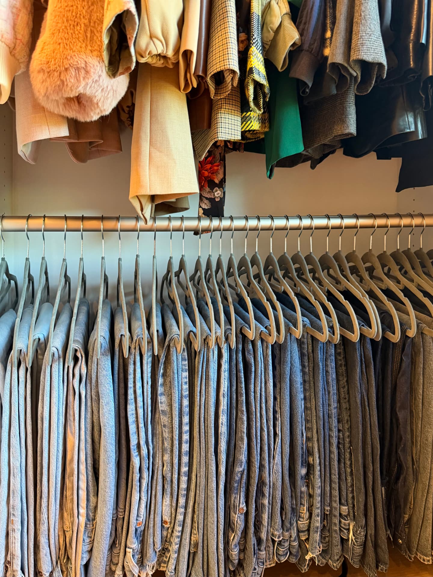 Close view of jeans hung neatly on hangers beneath a rail of jackets and sweaters
