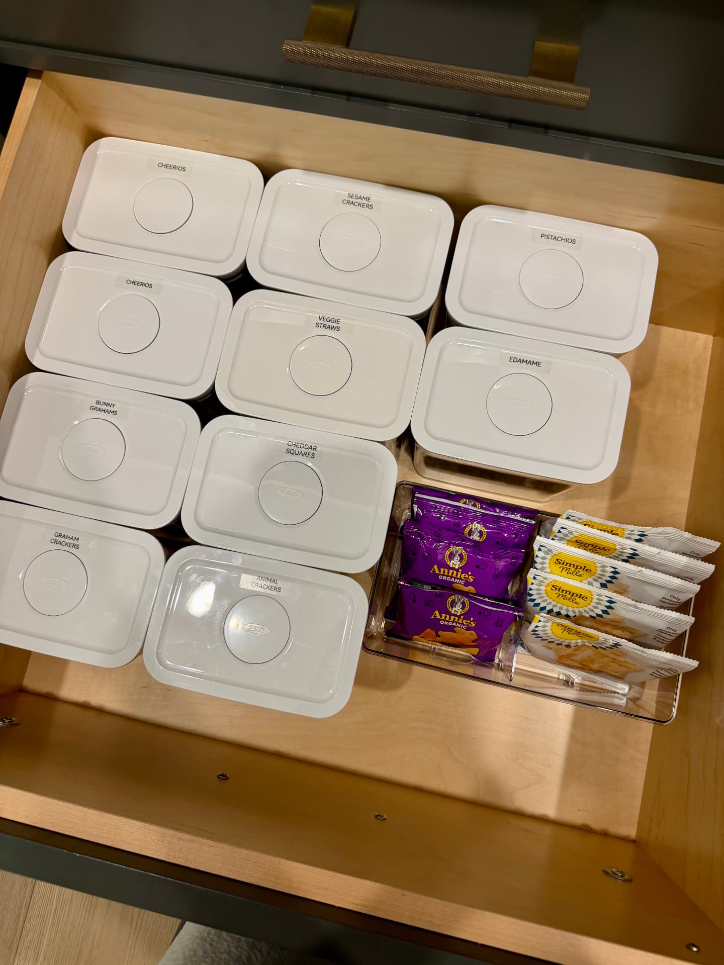 Open pantry drawer of OXO pop containers labeled with snacks like Cheerios, graham crackers, pistachios, and edamame