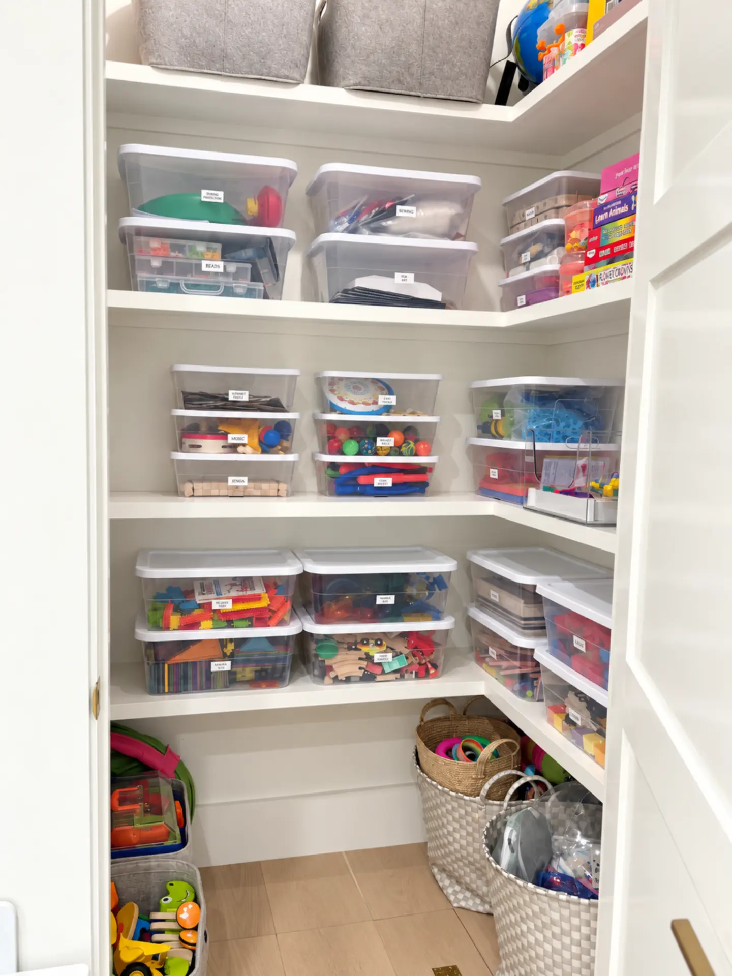 Corner shelves of the playroom closet with stacked labeled bins of games, music toys, puzzles, and blocks