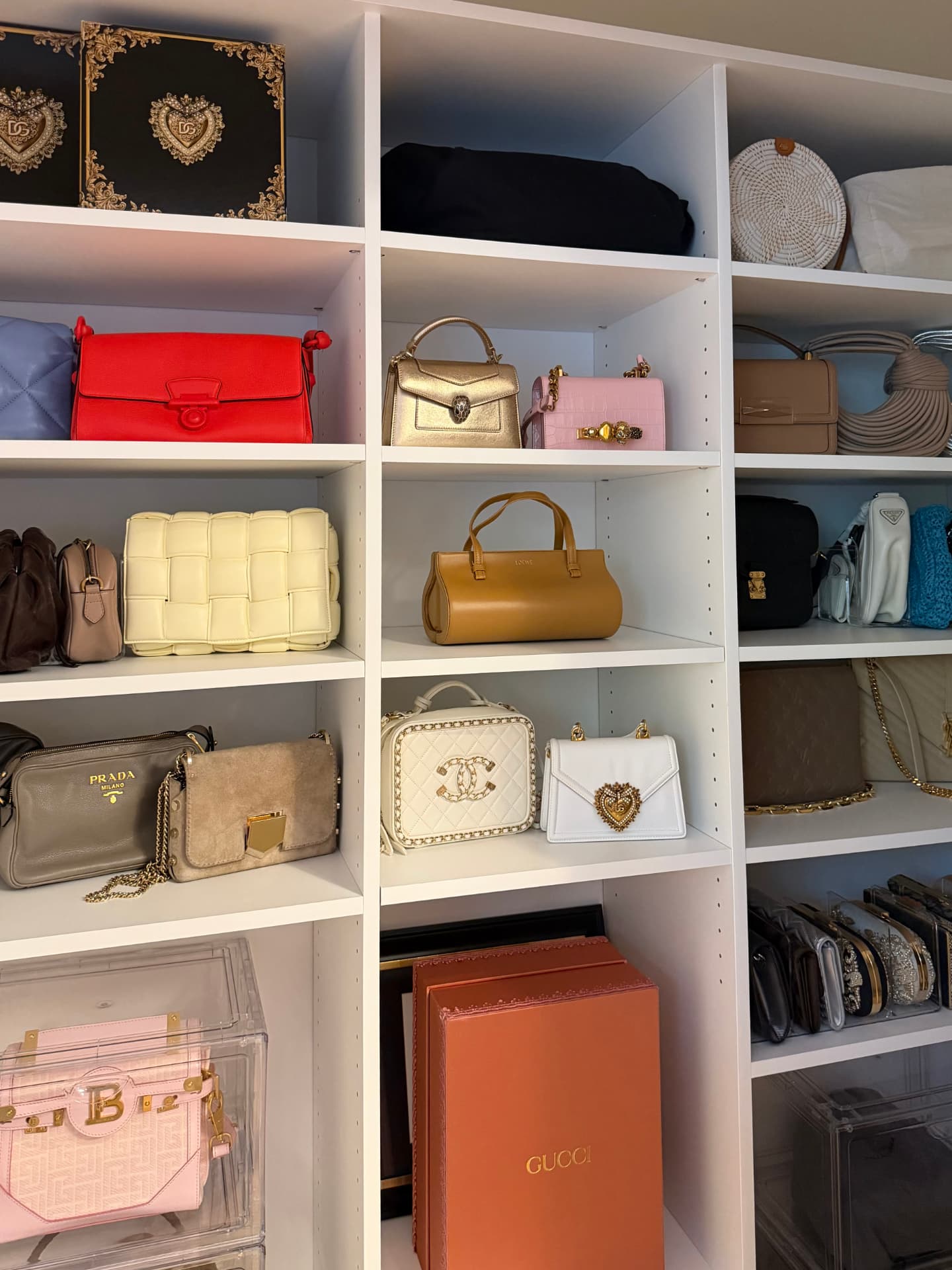 White shelving displaying designer handbags in rows, with hat boxes and storage boxes above and clear cases below